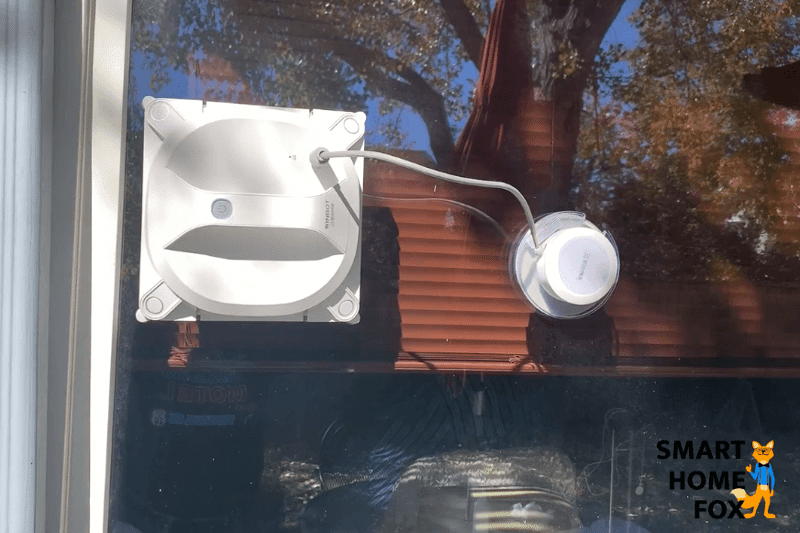 Man sieht den automatischen Fensterputzer Ecovacs Winbot X an einer Fensterscheibe.